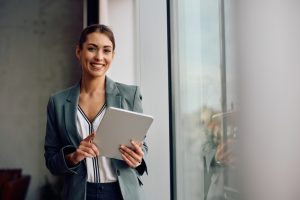 Happy female entrepreneur using touchpad while working in the office and looking at camera. Copy space.